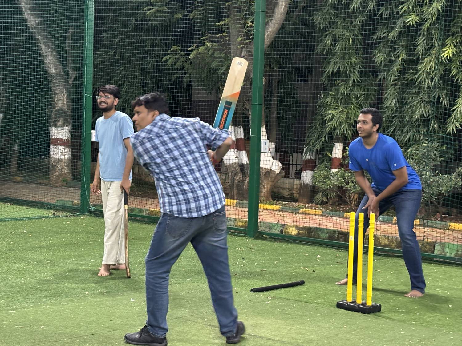 A tiramai team member swinging the bat while a teammate keeps wicket and another looks on
